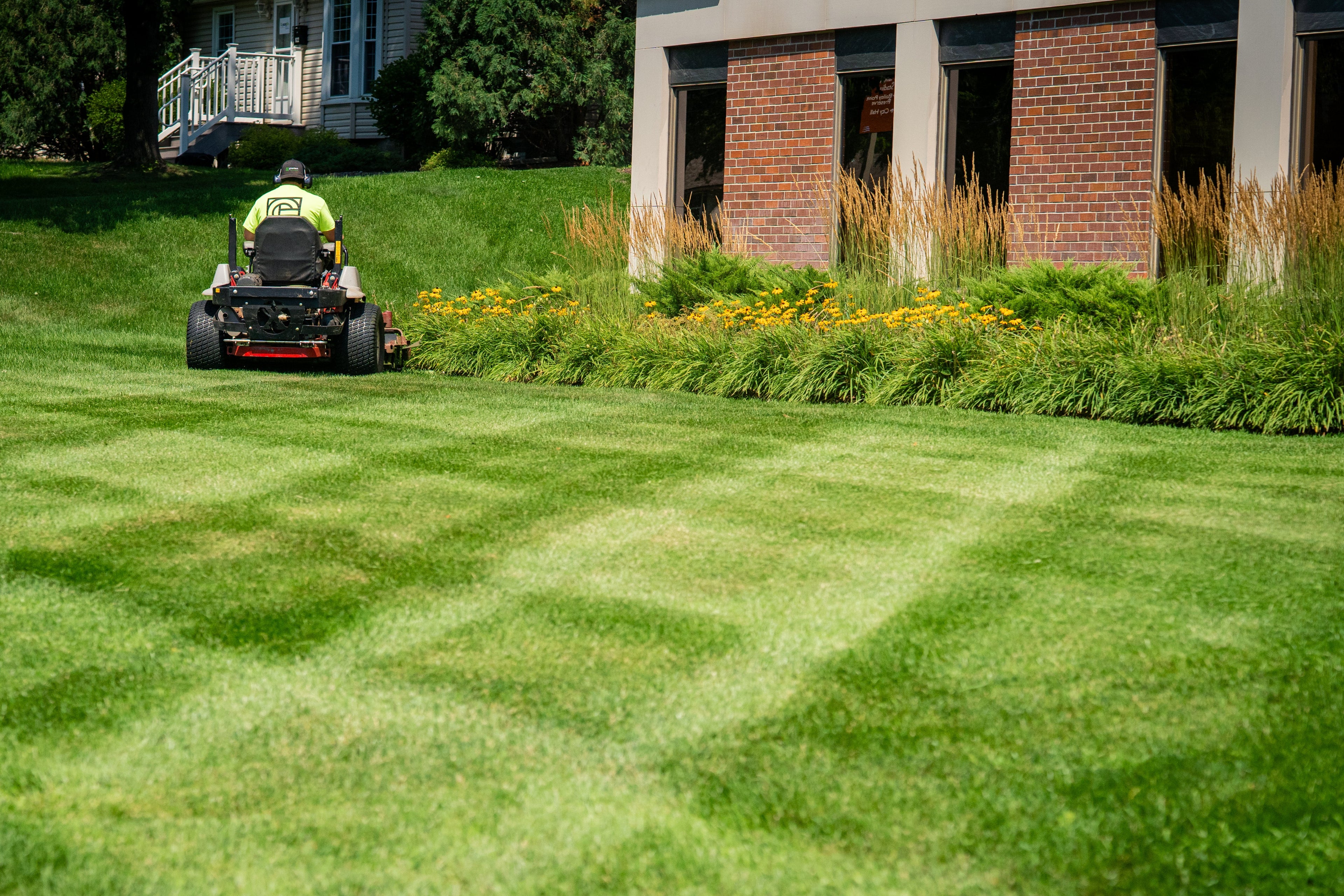 Person mowing a lawn with a riding mower in a commercial area.